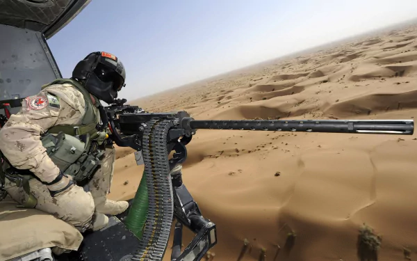 A soldier in tactical gear operates a machine gun from a helicopter, overlooking vast desert landscapes. This high-definition image captures a moment of military readiness.