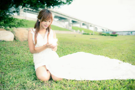 Taiwanese model Xiao Xi in a white dress kneeling on grass near a bridge, captured in 4K Ultra HD for a PC desktop wallpaper and background.