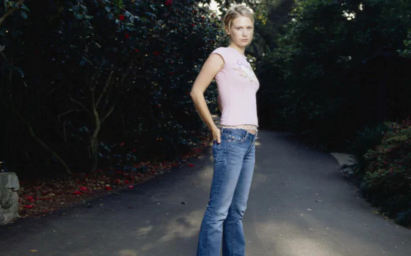 HD PC desktop wallpaper of a blonde female celebrity in a pink tank top and jeans standing on a shaded, tree-lined path.
