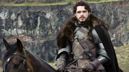 Richard Madden as Robb Stark, dressed in medieval attire, sits confidently on a horse against a dramatic backdrop, capturing a moment from the TV show Game of Thrones.