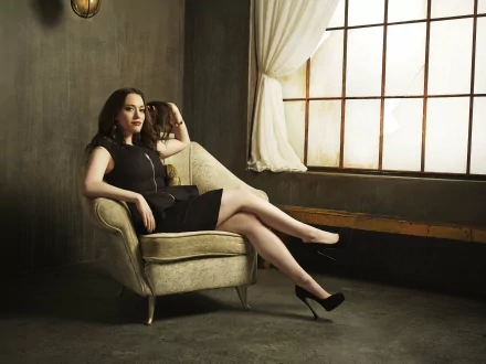 Brunette American actress Kat Dennings in a black dress and lipstick, seated confidently on a vintage chair by a window, captured in 4K Ultra HD.