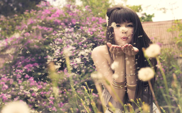 A woman with long hair playfully blows dandelion seeds in a vibrant garden filled with flowers, capturing the essence of spring in Pretoria, Africa.
