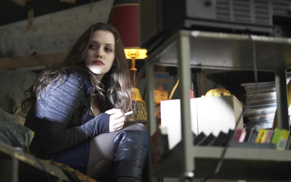 HD PC desktop wallpaper featuring celebrity Kat Dennings in a dimly lit, industrial-style setting with moody lighting and a contemplative expression.