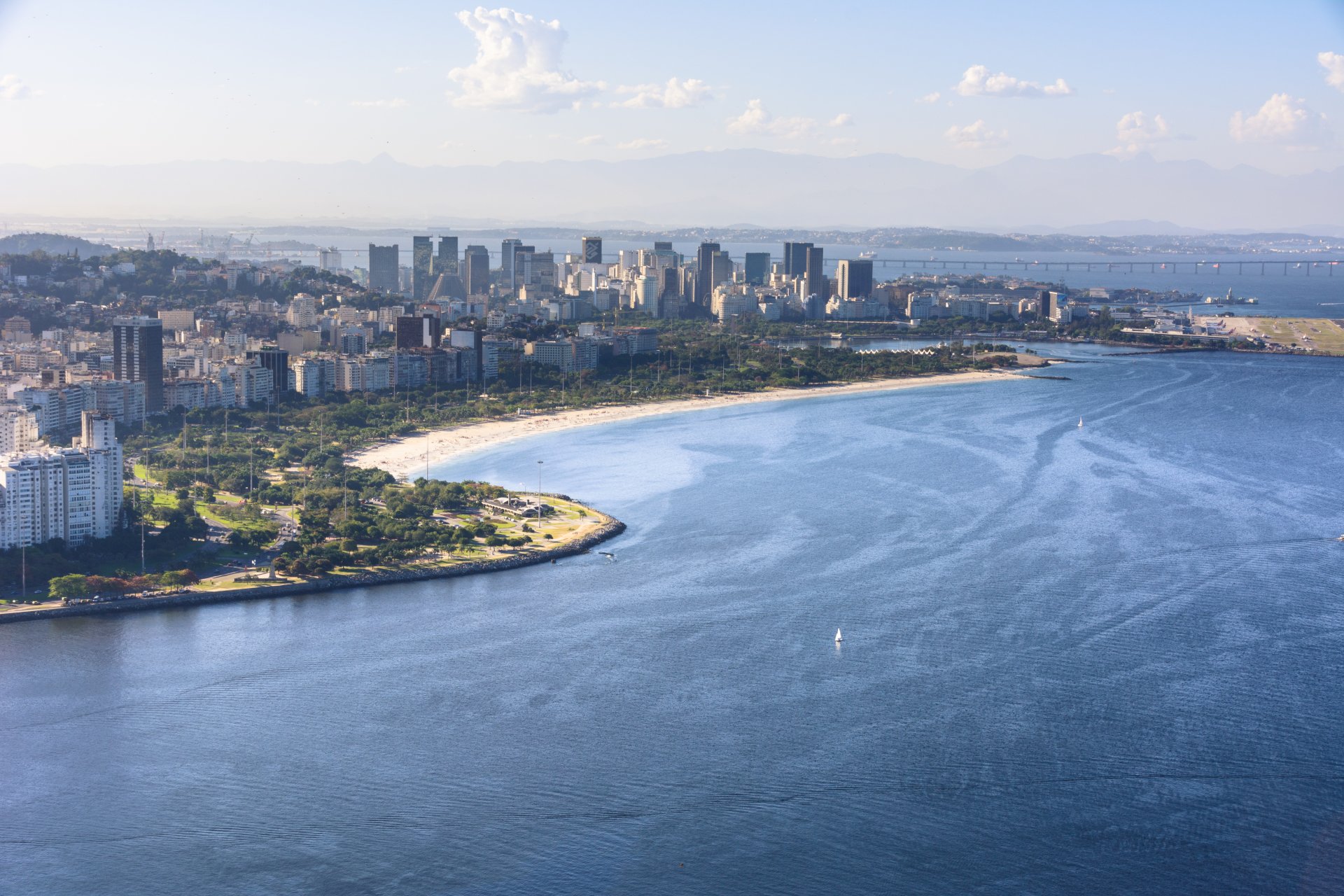 A 4K Ultra HD aerial view of the man-made beach in Rio de Janeiro, Brazil, showcasing the shoreline, cityscape, and calm blue waters.