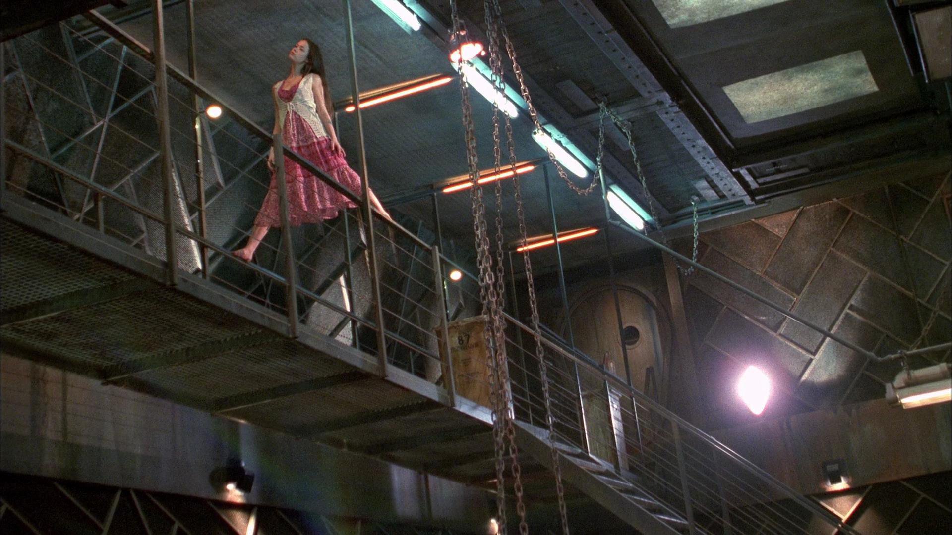 Serenity (2005) movie HD PC desktop wallpaper and background: woman in a pink dress walks a metal catwalk inside the ship, industrial interior lit by harsh, dramatic lights.