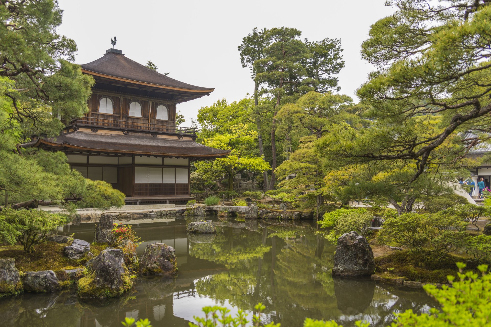 A serene zen garden at Ginkaku-ji (Temple of Shining Mercy) in Kyoto, Japan, showcasing traditional architecture and lush greenery reflected in a tranquil pond.