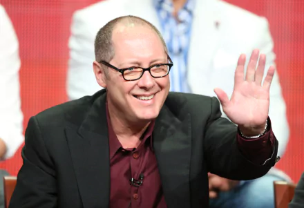 HD wallpaper of a man in a dark suit and glasses waving, with a blurred background.