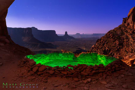 Twilight over Monument Valley canyon in Utah features a glowing green desert pool under a clear sky, captured in this striking HD desktop wallpaper.