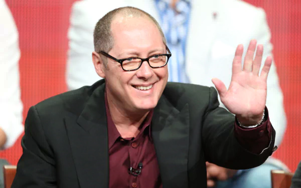 HD wallpaper of a man in a dark suit and glasses waving, with a blurred background.