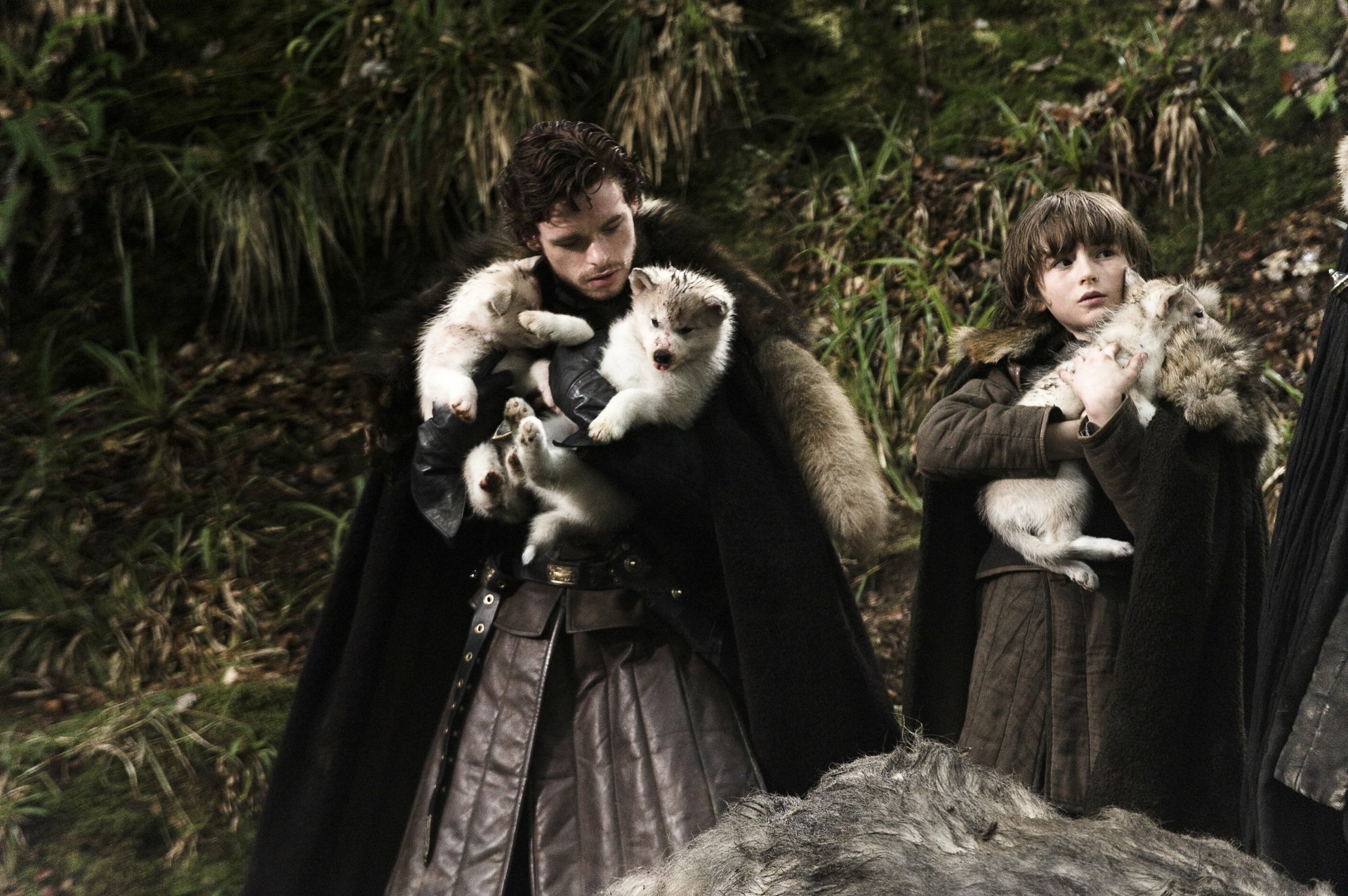 HD desktop wallpaper from Game of Thrones featuring Kit Harington as Jon Snow holding direwolf pups in a forest setting.