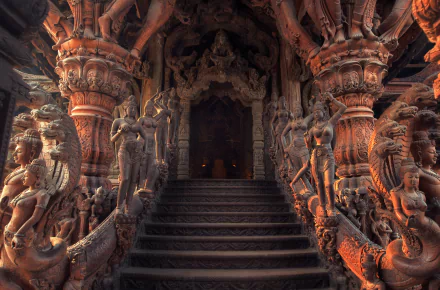 Intricate wooden statues adorn the entrance of the Sanctuary of Truth in Thailand, showcasing exquisite craftsmanship in a religious setting, leading to the majestic Prasat Mai.