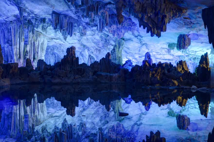 5K Ultra HD wallpaper: luminous Reed Flute Cave interior in Guangxi Zhuang, China — stalactites and stalagmites bathed in blue light, mirrored perfectly in a glassy underground pool.