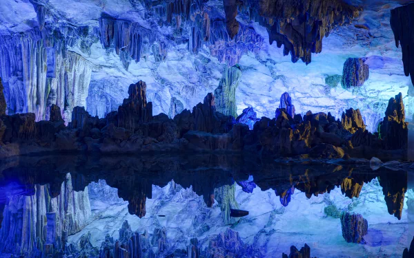 5K Ultra HD wallpaper: luminous Reed Flute Cave interior in Guangxi Zhuang, China — stalactites and stalagmites bathed in blue light, mirrored perfectly in a glassy underground pool.
