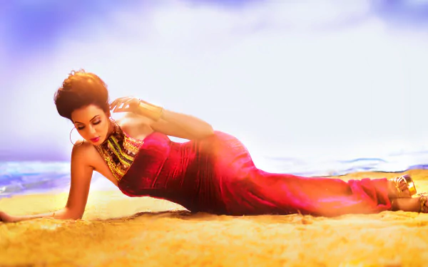 A woman in a colorful red Indian dress lies on sand under a cloudy sky, captured in HD as a striking desktop wallpaper by Malvika Rallan.