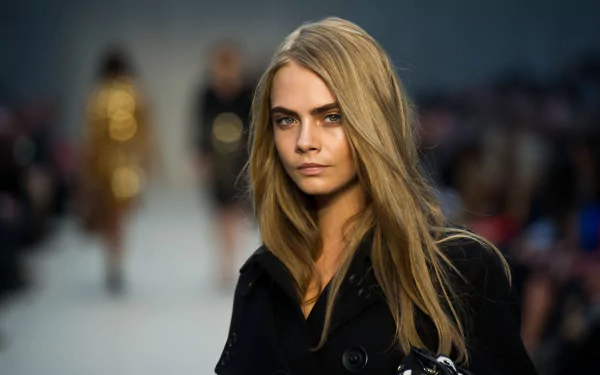 A stylish Cara Delevingne with blue eyes and blonde hair walks confidently on the runway, embodying fashion and celebrity allure in a striking 4K Ultra HD background.