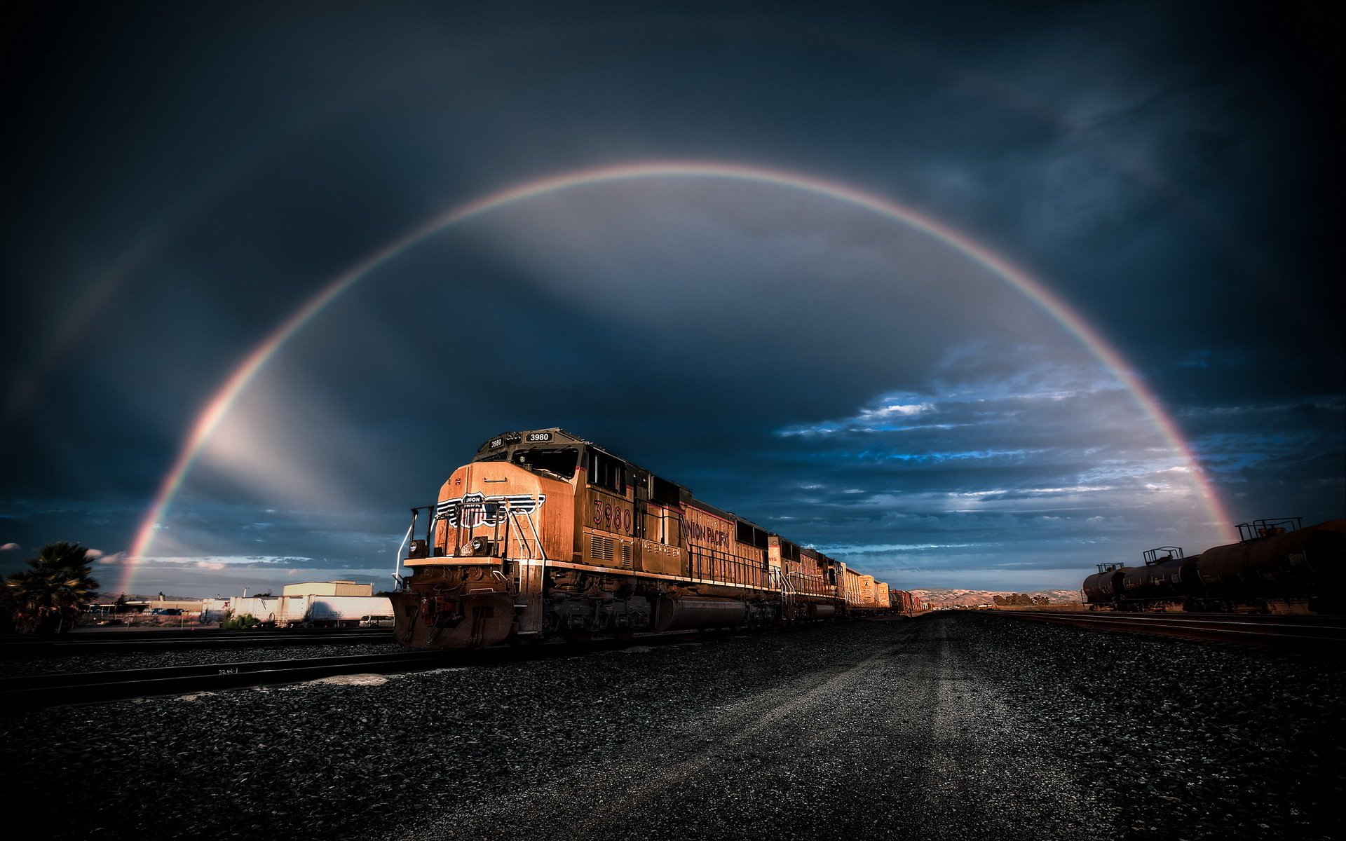 A striking HD desktop wallpaper featuring a train against a dramatic sky, highlighted by a vibrant rainbow, capturing the essence of travel and nature.