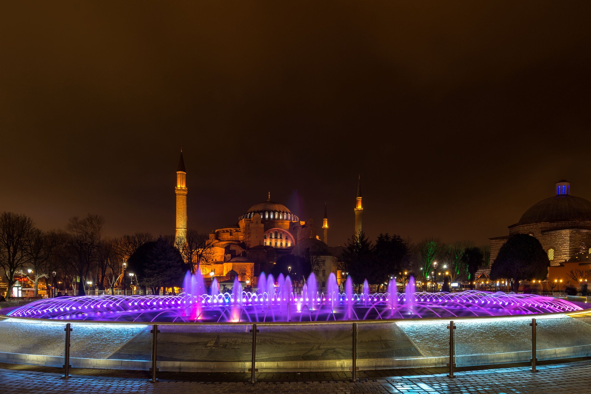 A vibrant fountain illuminated with colorful lights in front of the Hagia Sophia mosque, showcasing Istanbul's beauty at night in Turkey. A stunning 4K Ultra HD wallpaper.