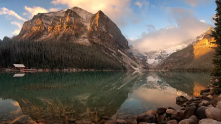 HD PC desktop wallpaper capturing the serene beauty of Lake Louise with calm waters reflecting majestic mountains under a partly cloudy sky.