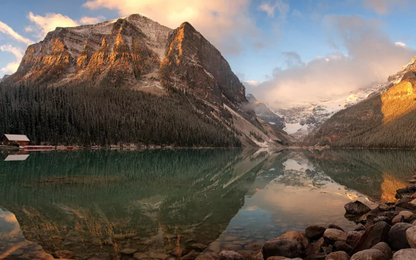HD PC desktop wallpaper capturing the serene beauty of Lake Louise with calm waters reflecting majestic mountains under a partly cloudy sky.
