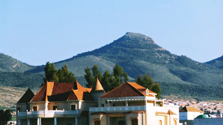 4K Ultra HD image showcasing a villa in a town with the Tebessa Mountains of Algeria towering in the background under a clear blue sky.