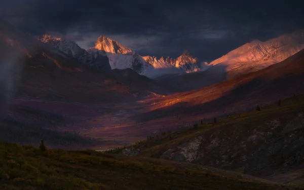 HD desktop wallpaper of the Yukon tundra at sunrise, showcasing rugged Canadian mountains bathed in warm morning light beneath a dramatic sky.
