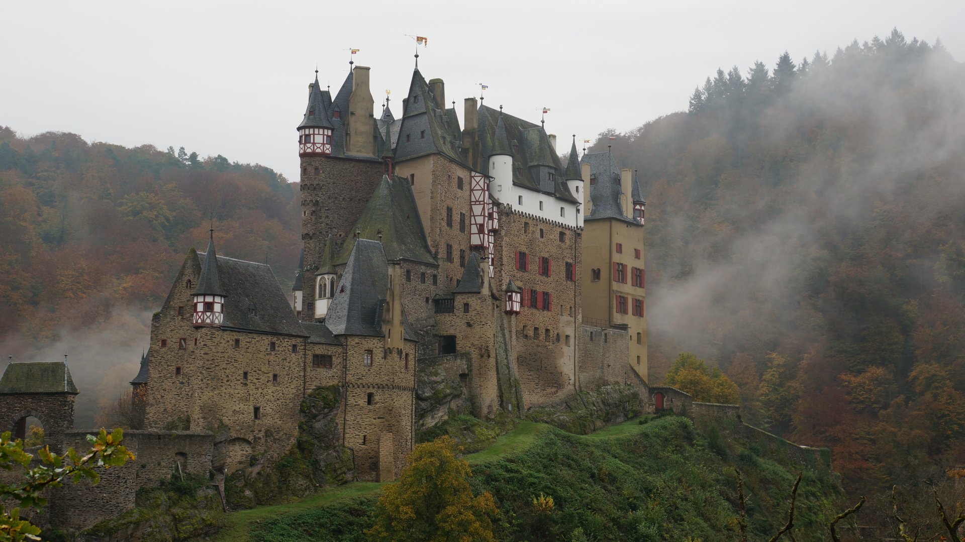 Fog-shrouded Eltz Castle in Germany, man-made stone turrets rising above autumn woods — 4K Ultra HD PC desktop wallpaper background.