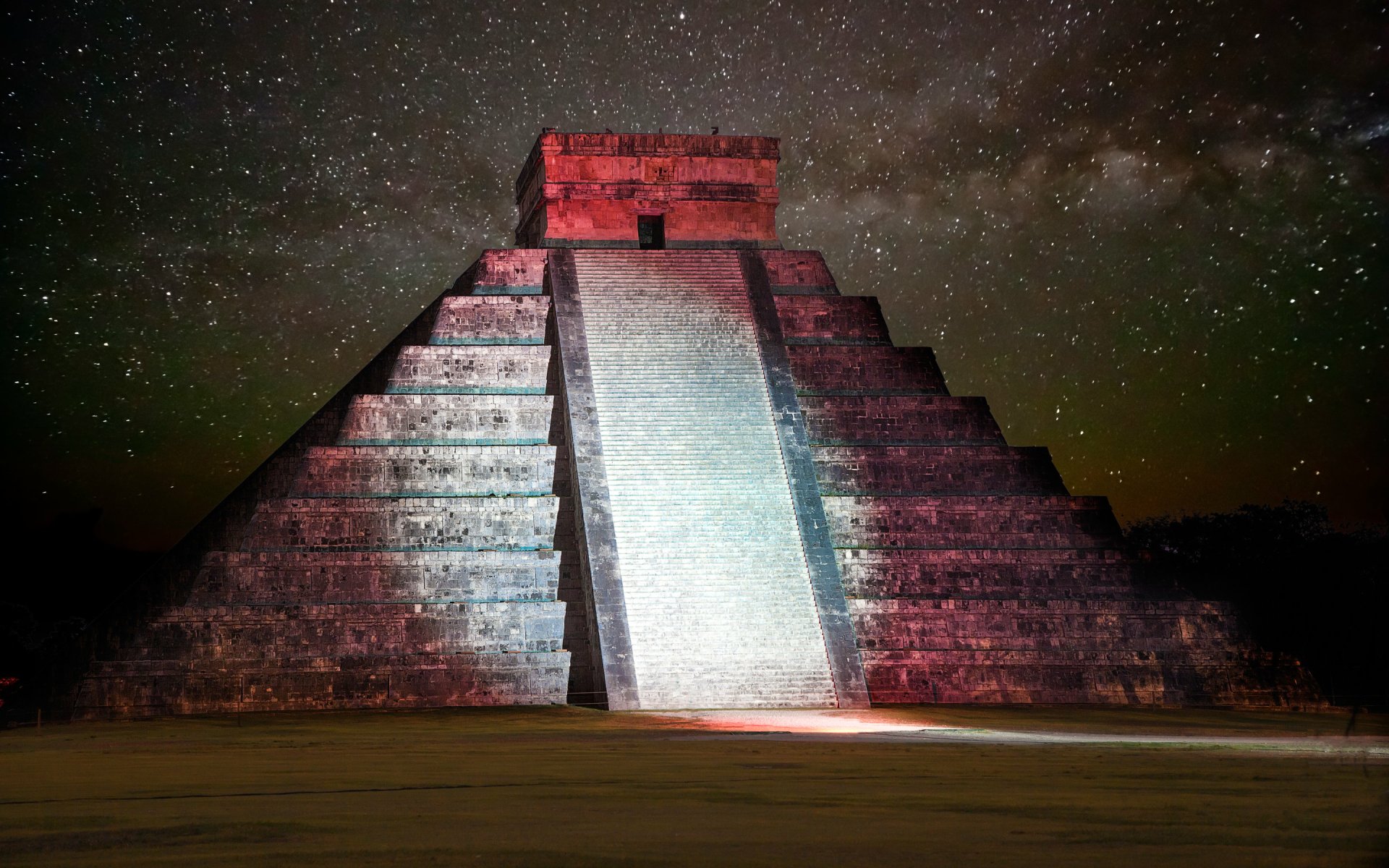 Chichen Itza pyramid in Mexico illuminated at night under a starry sky, showcasing its ancient man-made structure with vibrant lighting.