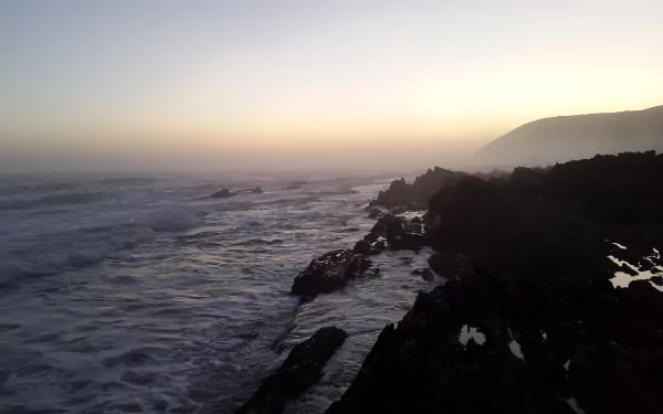 A serene 4K Ultra HD seascape of South Africa’s coastline at the cape, with waves crashing against rocky shores under a soft, muted sky.