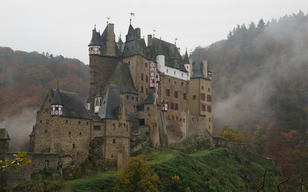 Fog-shrouded Eltz Castle in Germany, man-made stone turrets rising above autumn woods — 4K Ultra HD PC desktop wallpaper background.