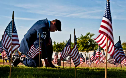 A service member kneels among American flags in a Memorial Day tribute, captured in 4K Ultra HD as a patriotic holiday desktop wallpaper.