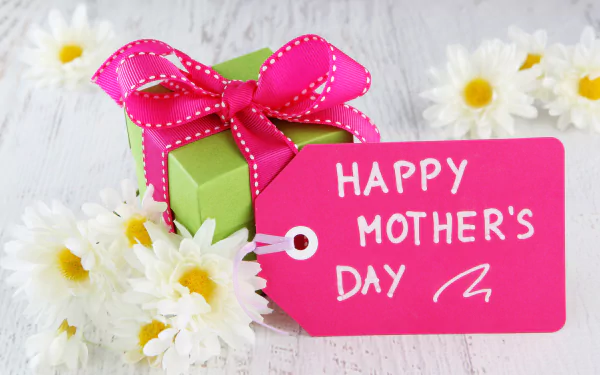 A cheerful Mother's Day gift box with a bright pink ribbon and tag reading Happy Mother's Day, surrounded by white daisies, creating a festive holiday atmosphere.