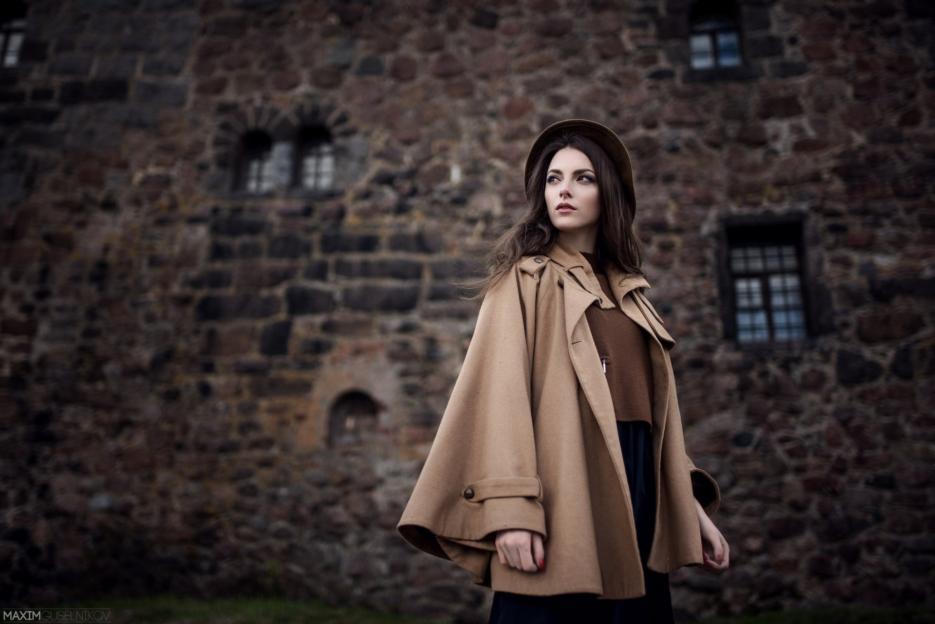 A vintage-style portrait of a woman model Karina Sunceva wearing a retro hat and beige coat, standing against a historic stone building in Russia, HD desktop wallpaper.