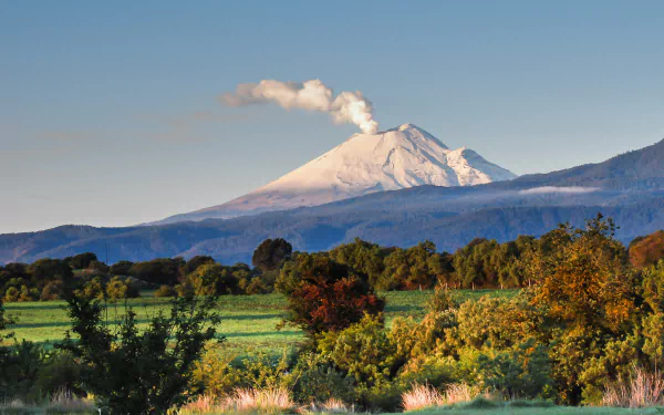 A stunning view of Popocatépetl, an erupting volcano in Mexico, surrounded by lush greenery and mountains, captured in vibrant detail as a desktop wallpaper.