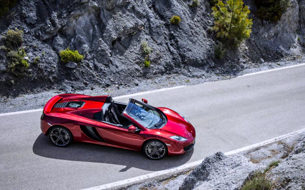 A striking red McLaren MP4-12C Spider glides along a winding road, showcasing its sleek design and impressive engineering in this 4K Ultra HD wallpaper.