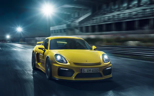 Yellow Porsche Cayman GT4 speeding on a racetrack at night, showcased as an HD PC desktop wallpaper and background.
