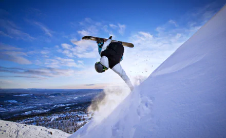 A snowboarder executes a trick on a snowy slope under a bright blue sky, capturing the essence of winter sports in this stunning 4K Ultra HD wallpaper.