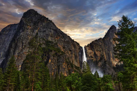 Bridalveil Fall cascades down rugged cliffs in Yosemite National Park, California, surrounded by dense forest under a dramatic sky in this 8K Ultra HD desktop wallpaper.