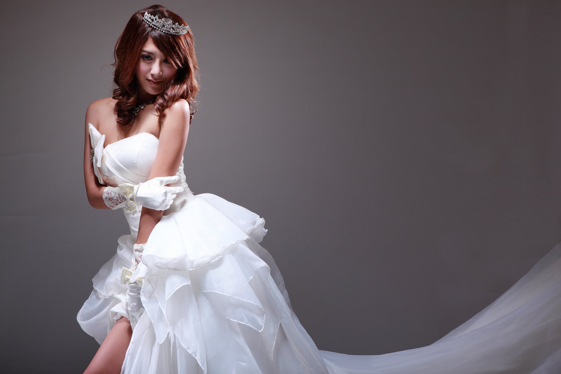 Studio portrait of a bridal model in a flowing white wedding dress, diadem and elbow gloves, posing against a neutral backdrop — 5K Ultra HD desktop wallpaper.
