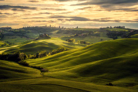 Rolling green hills of Tuscany under a dramatic cloud-filled sky, showcasing the natural beauty of Italy in this HD landscape photography wallpaper.