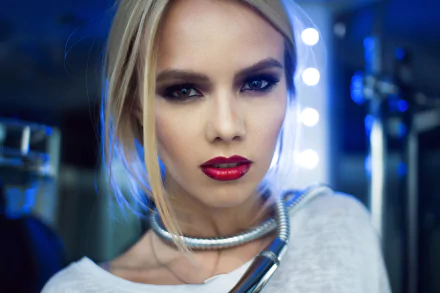 Close-up HD desktop wallpaper of a blonde woman model with striking brown eyes and bold red lipstick, her face illuminated by soft, cool lighting.