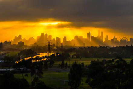 A stunning Melbourne cityscape at sunset, bathed in golden sunlight with dramatic clouds. Power lines stand silhouetted against the skyline, creating a striking contrast in this HD wallpaper.