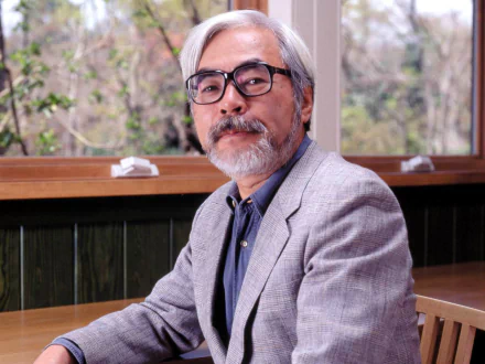 HD desktop wallpaper featuring Hayao Miyazaki seated in a room with a wooden interior, presenting a calm and thoughtful appearance.