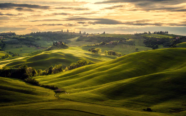 Rolling green hills of Tuscany under a dramatic cloud-filled sky, showcasing the natural beauty of Italy in this HD landscape photography wallpaper.
