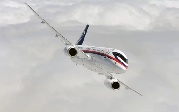 Sukhoi SuperJet 100 jet airplane flying above clouds, captured in a high-definition desktop wallpaper showcasing the sleek design of this modern aircraft in flight.