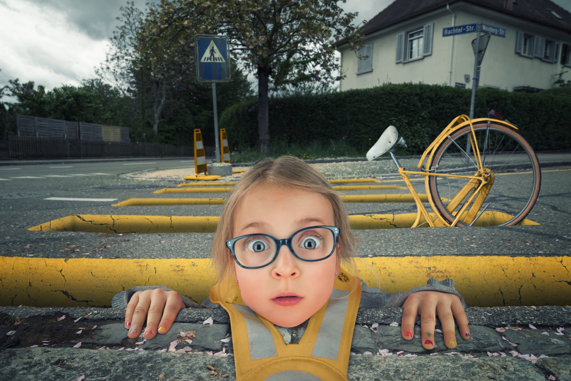 Humorous manipulated street photo: a wide-eyed child appears stuck between yellow barriers beside a fallen yellow bicycle — HD PC photography desktop wallpaper/background.