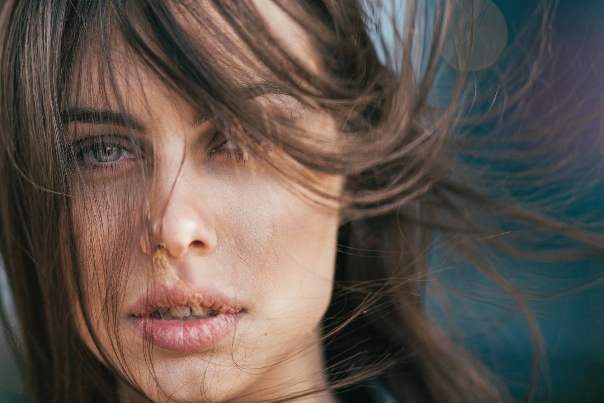 Close-up of a brunette model with striking blue eyes and windblown hair, captured in high-definition for a PC desktop wallpaper background.
