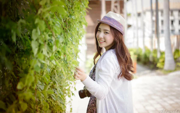 A smiling Taiwanese Asian woman model, Chén Sīyǐng, wearing a hat, captured in 4K Ultra HD with a shallow depth of field, holding a camera outdoors.