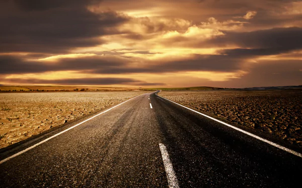 A HD wallpaper of a desert road stretching into the horizon under a dramatic cloud-filled sky at sunset.