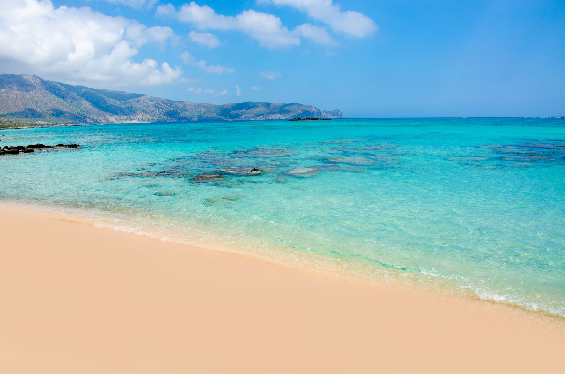 4K Ultra HD PC desktop wallpaper — nature seascape: pale sandy beach, crystal turquoise water and rocky reefs with distant hills beneath a bright blue sky.