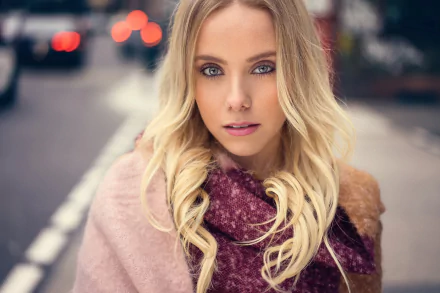 HD desktop wallpaper features a blonde model with striking blue eyes against a softly blurred bokeh city background.